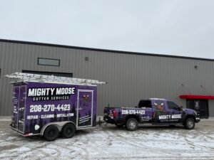 Mighty Moose Gutter Services wrapped truck and ladder-topped enclosed trailer parked outside a shop