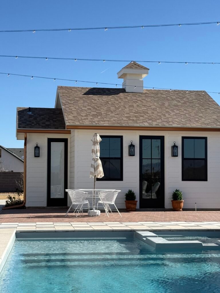 Backyard poolhouse casita with shingle roof and copper-toned downspout beside an in-ground pool